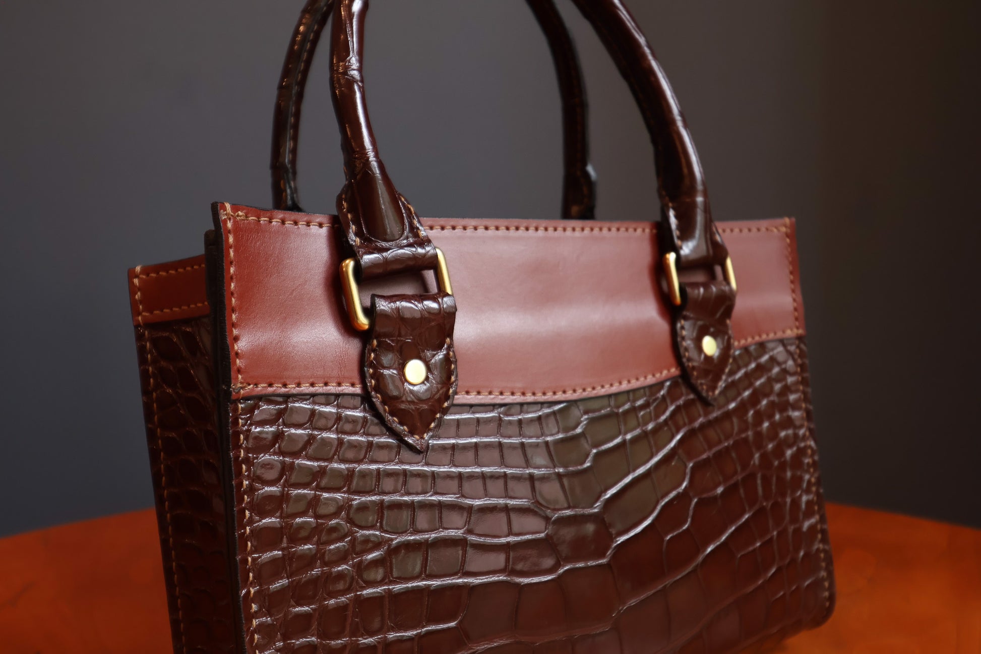 The Darlington handbag by Garrett Wayne - detail view of rolled alligator leather handles, cognac trim, and brass buckle hardware